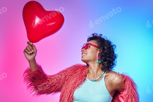Preview: Beautiful African woman in trendy clothes carrying red balloon and smiling