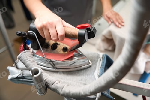 Vista previa: Woman laundry office operator taking hot iron with steam to remove wrinkles