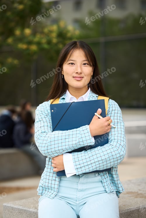 Preview: Chinese student at campus university wearing a blue jacket and jeans is holding a blue book