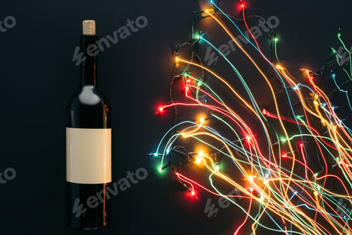 Preview: elevated view of wine bottle and garland lights with long exposure isolated on black, christmas