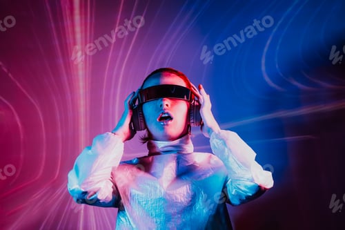 Preview: Portrait of dancing woman in futuristic sunglasses and headphones in pink and blue neon light.