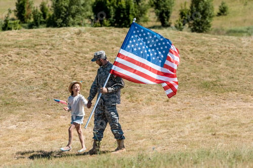 Preview: military man and happy patriotic kid holding hands and american flags