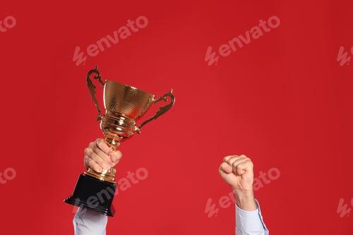 Preview: Young man with gold trophy cup on red background, closeup. Space for text