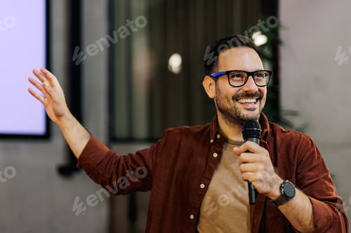 Aperçu: Homme heureux prononçant un discours, tenant un microphone, pointant du doigt un écran de projection.