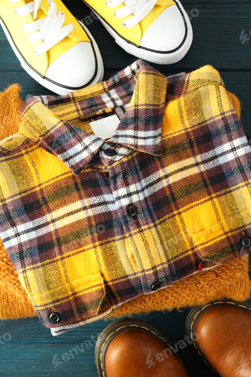 Preview: Shirt, sweater, sneakers and boots on wooden table