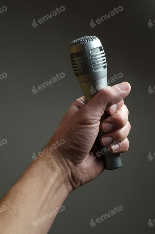 Preview: Person grasping a handheld microphone in their right hand on a gray background