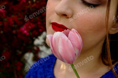 Preview: Minimalistic portrait of young female with eyes closed tilting her head holding a tulip near face.