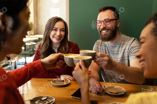 Preview: Happy friends toasting cappuccino cups in a cafe