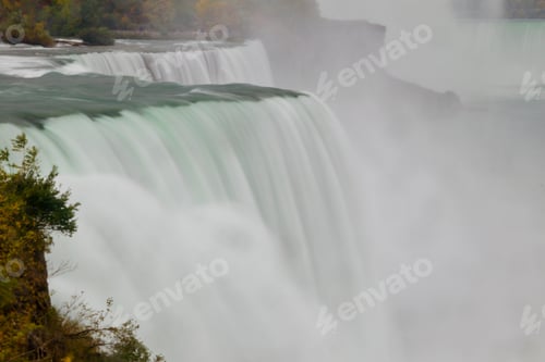 Vorschau: Nebeliger Blick auf den Wasserfall mit den herbstlichen Bäumen am Flussufer