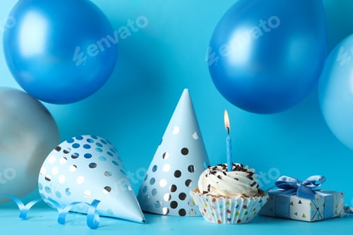 Preview: Balloons, birthday hats, cupcake and gift box on blue background, close up