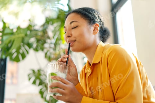 Preview: Smiling beautiful African American woman drinking drinking fresh tasty lemonade in cafe