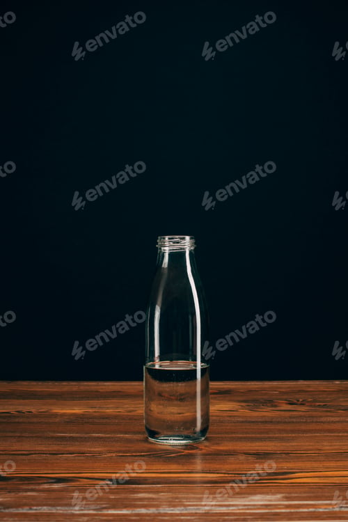 Preview: glass bottle with mineral water on brown table on black