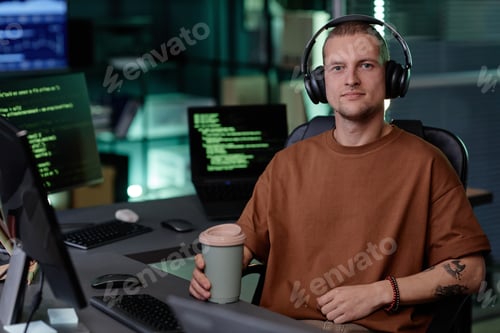 Preview: Portrait of Male IT Developer in Headphones Sitting at Desk with Coffee in Office