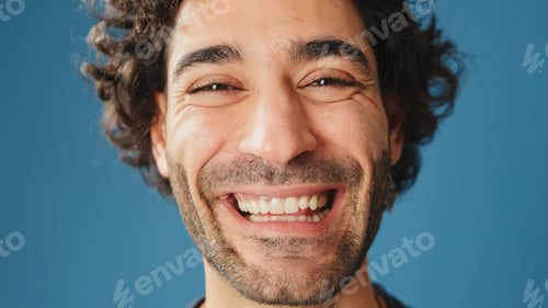 Preview: Close-up, man opens his eyes smiling and looking at camera isolated on blue background in studio