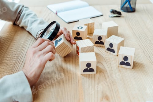 Preview: cropped view of recruiter holding magnifier near cube in office