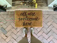 Preview: “All are welcome here” entrance rug door mat & flowers at house’s door.