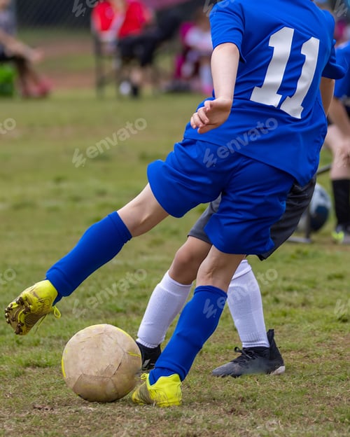 Preview: Young boy wearing a blue jersey is kicking a soccer ball on a soccer field