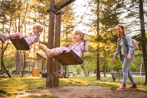 Preview: Mother is rocking her twin daughters on a swing in the park