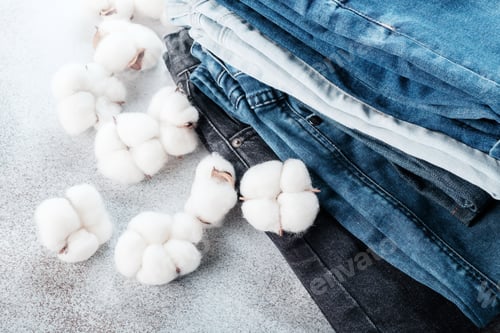 Preview: Stack of jeans pants and cotton flowers on light background