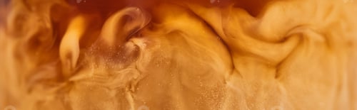 Preview: close up view of brown coffee mixing with white milk in glass, panoramic shot