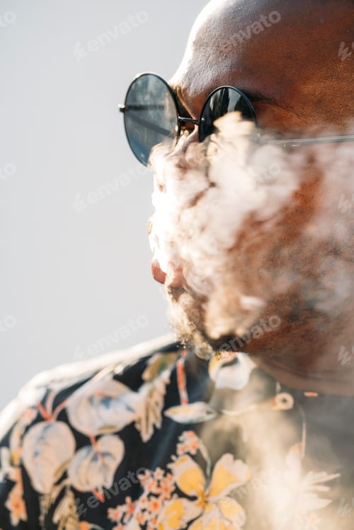 Preview: Black stylish man wearing sunglasses. He is vaping with an electronic cigarrete outdoor
