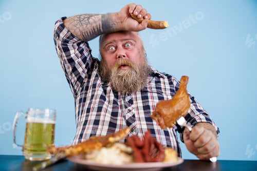 Preview: Tired obese man mops brows suffering from overeating at table with fat food in studio