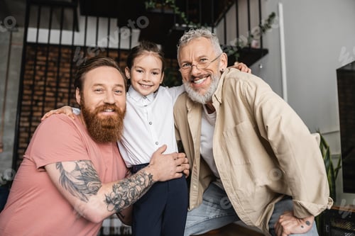 Preview: Smiling lgbt couple looking at camera and hugging adopted daughter at home