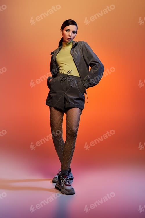 Preview: Fashionable young woman poses confidently in stylish outfit against orange backdrop
