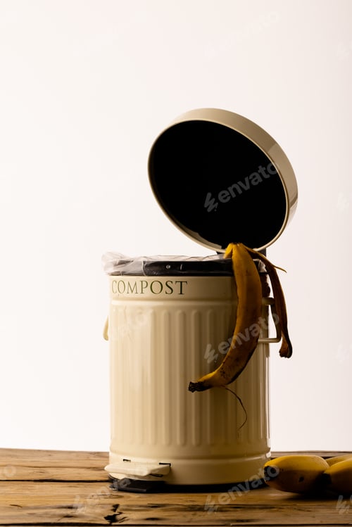 Preview: Vertical image of banana skin hanging out of open kitchen composting bin