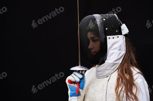 Preview: Portrait of woman dressed in fencing costume on black background.