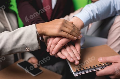 Preview: cropped view of business team holding hands together in front of green wall