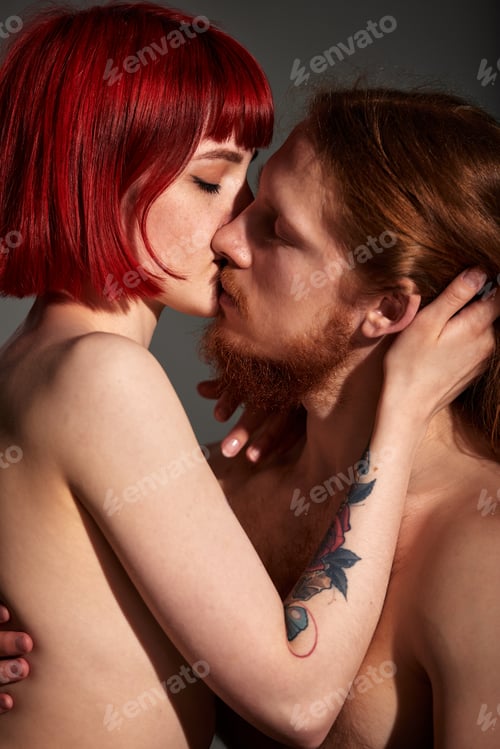 Preview: Young attractive woman with bright ruby hair and tattoo hugs and kisses her man with long hair and