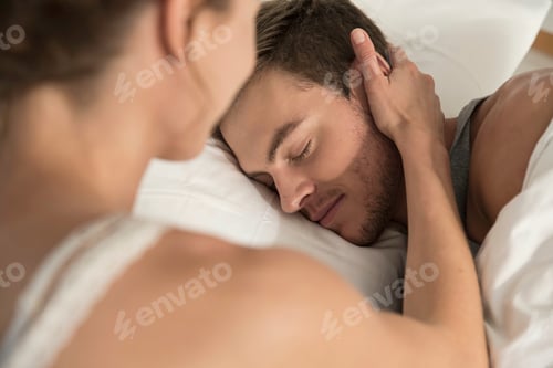 Preview: Young woman lying in bed touching sleeping boyfriends cheek
