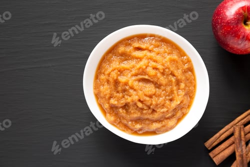 Preview: Homemade Raw Apple Sauce in a White Bowl on a black surface, top view. From above, flat lay.