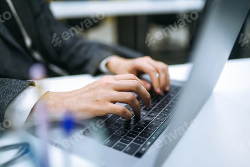 Preview: Close up of man hand working on laptop computer and writing on notebook on table at home office.