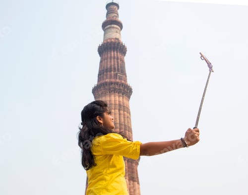 Preview: Tourist woman taking selfie in front of Qutub Minar, Delhi, India.