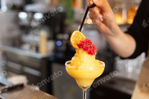 Preview: Preparation of frozen cocktail decorated with flowers and dried fruit with unfocused bar background