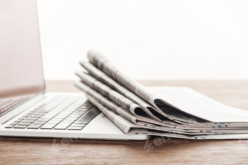Preview: laptop and stack of newspapers on wooden tabletop