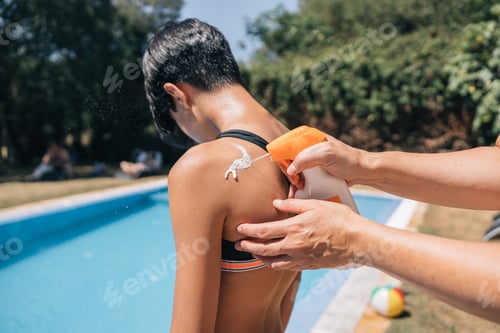 Preview: A mother applying sunscreen to her teenage daughter before sunbathing in the swimming pool