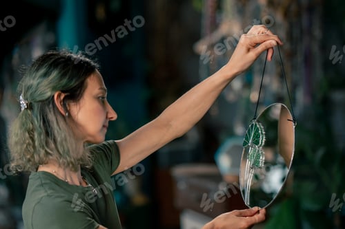 Preview: in a large green workshop, a woman with green hair has finished decorating a mirror with a glass
