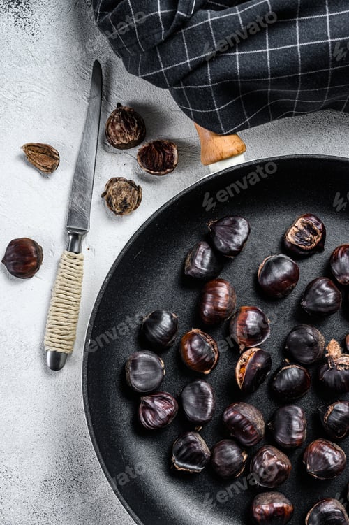 Preview: Fried chestnuts in a pan on a wooden table. White background. Top view