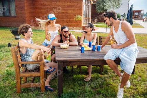 Preview: Group of happy young people sitting and drinking beer outdoors