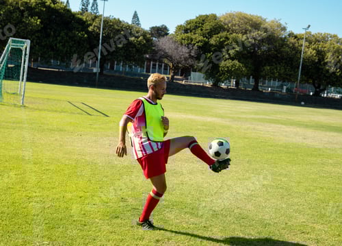Preview: Male soccer player controlling soccer ball on grass soccer field, with goalpost and fluorescent bib