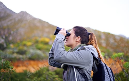 Preview: Shot of an attractive young woman looking through binoculars while on a hike