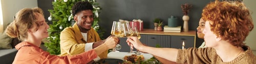 Preview: Diverse Young Adults Celebrating Christmas Toasting Drinks Around Festive Table
