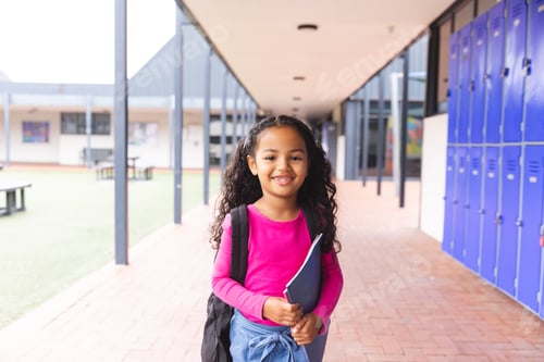 Preview: In school, young biracial female student holding a tablet stands smiling
