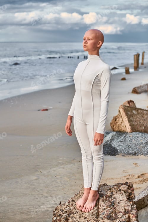 Preview: Full length portrait of hairless girl with alopecia in futuristic suit standing on seashore