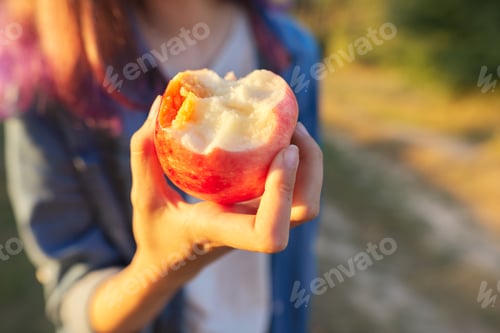 Preview: Tasty juicy eaten red apple in girls hand closeup, nature, sunset, golden hour