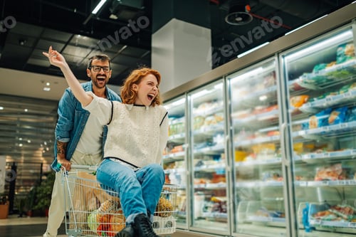 Preview: Happy couple having fun riding shopping cart in supermarket