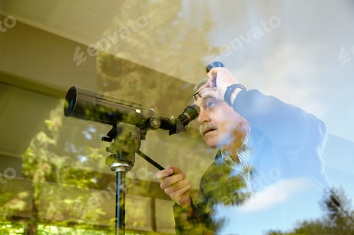 Preview: Senior man at home, using telescope through window